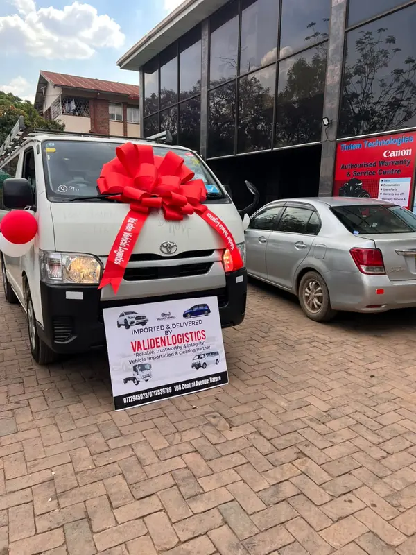 White Toyota HiAce van with a red delivery bow and the Validen &ldquo;Imported & delivered&rdquo; board