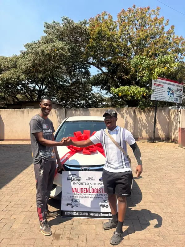 A client shakes hands on his white Honda Fit, red bow on the bonnet and the Validen board in front